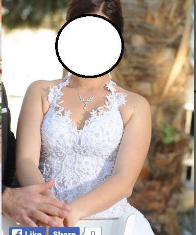 אדם בשמלת כלה לבנה ללא שרוולים יושב בחוץ, מחזיק ידיים עם מישהו. הרקע כולל גזע עץ דקל, היוצר סביבה טבעית ושלווה.