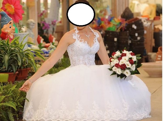 אדם בשמלת כלה לבנה תחרה מחזיק זר פרחים אדומים ולבנים. הם מוקפים בצמחים ירוקים ועיטורי גן צבעוניים.