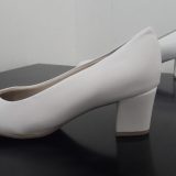 זוג נעליים לבנות עם עקב בלוק על משטח כהה, ממוקמות עם נעל אחת מול השנייה, על רקע בהיר רגיל.