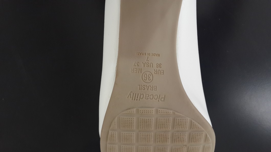 תקריב של סוליית נעל המציגה פרטי מידה ומקור. בטקסט כתוב EU 36, USA 5 1/2, Made in Brazil, Piccadilly. הסוליה בצבע חום בהיר עם דוגמת רשת בחלק התחתון, על רקע שחור.