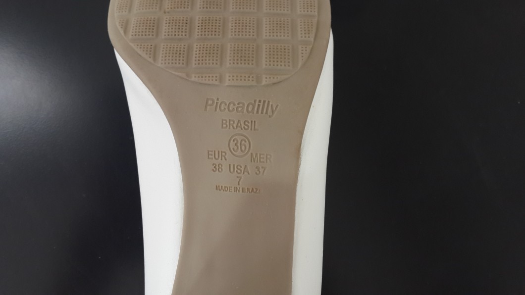תחתית נעל לבנה המציגה את המותג פיקדילי ופרטי מידה: 36 אירו, MER 38, ארהב 37, ו-7. תוצרת ברזיל מוטבעת למטה. הסוליה כוללת דפוס מרקם על רקע שזוף.