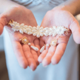 אדם מחזיק צמיד פנינים עדין מעוטר בעיצובים בצורת פרחים וזוג עגילי פנינים. התכשיטים מעורסלים בעדינות בשתי כפות ידיים פתוחות, עם רקע מטושטש.