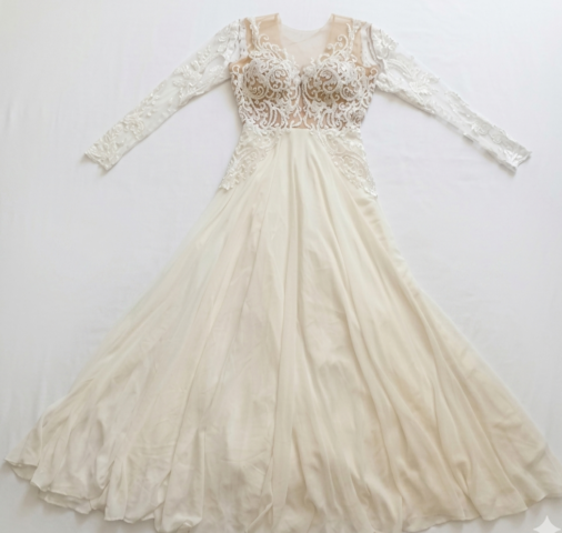 שמלת ערב אלגנטית בצבע שנהב, בעלת שרוולים ארוכים, עם מחוך שקוף, עיטורי תחרה וחרוזים מורכבים בחלק העליון, וחצאית שיפון מתנפנפת הפרושה על משטח לבן.