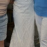 שלושה אנשים מצטלמים יחד; המוקד הוא על האישה שבמרכז, הלובשת שמלת ערב לבנה עם חרוזים ודוגמת גיאומטרית, בעלת כתפיות דקיקות. שני האחרים נראים חלקית, לבושים בבגדים יומיומיים.