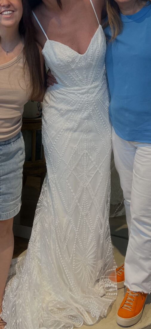 שלושה אנשים מצטלמים יחד; המוקד הוא על האישה שבמרכז, הלובשת שמלת ערב לבנה עם חרוזים ודוגמת גיאומטרית, בעלת כתפיות דקיקות. שני האחרים נראים חלקית, לבושים בבגדים יומיומיים.